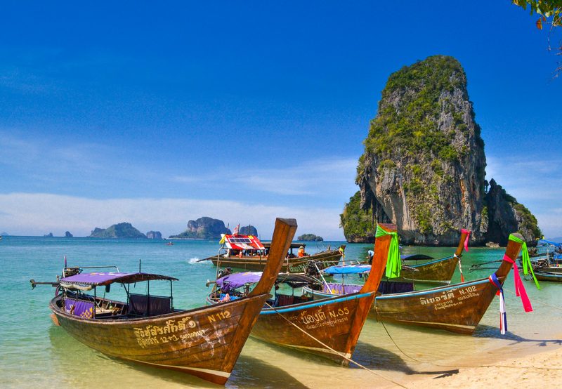 Traditional Thai longtail boats moored on a turquoise beach with limestone karsts
